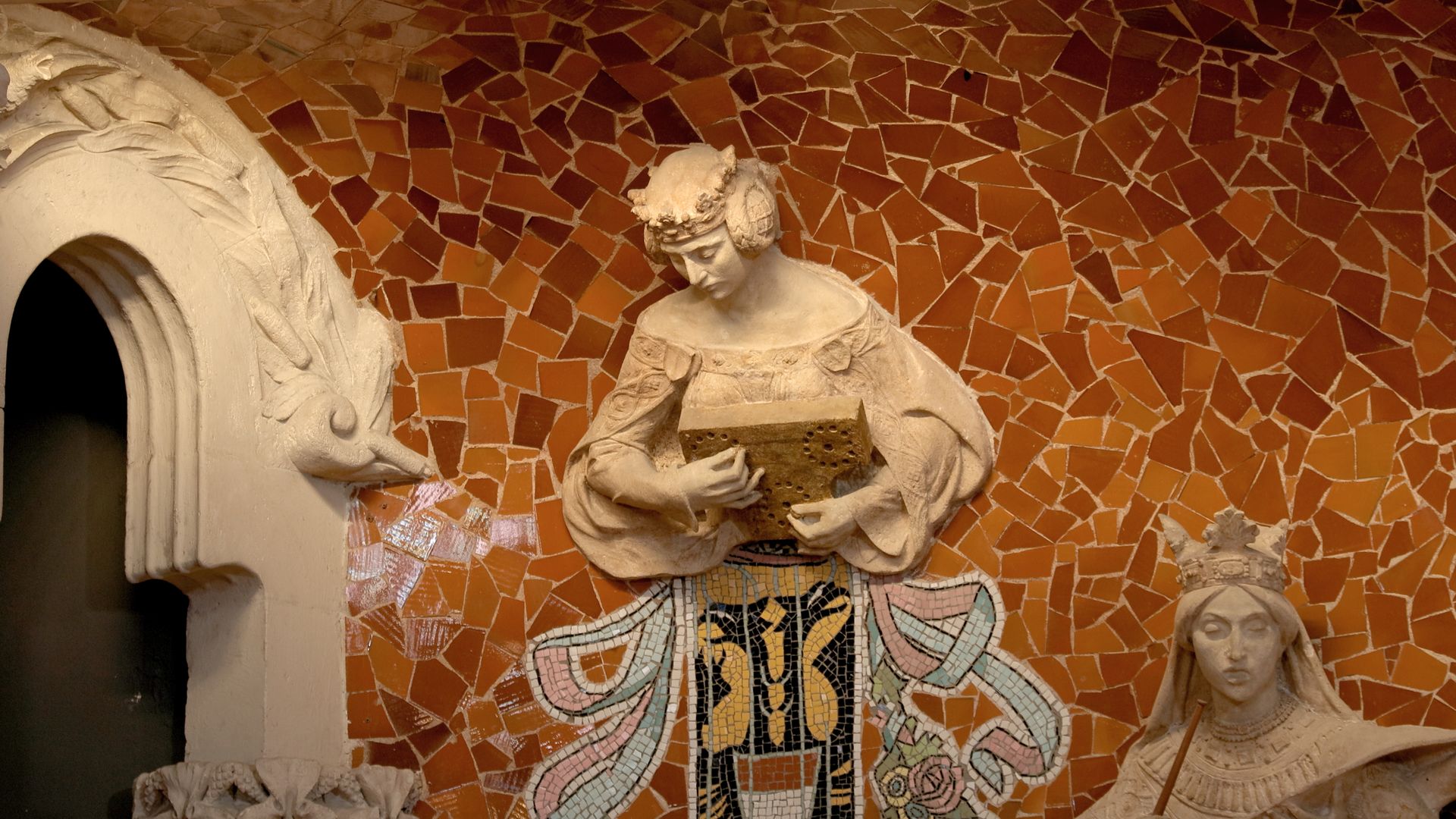 MUSES: a sculpted muse holding a book against the orange trencadís mosaic of the Palau de la Música Catalana